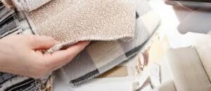 Hand holding a beige textured rug with a checkered rug underneath.